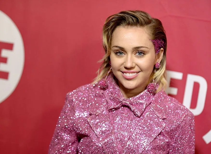 Η Miley Cyrus με ροζ αστραφτερό σακάκι και γκλίτερ στα μαλλιά.