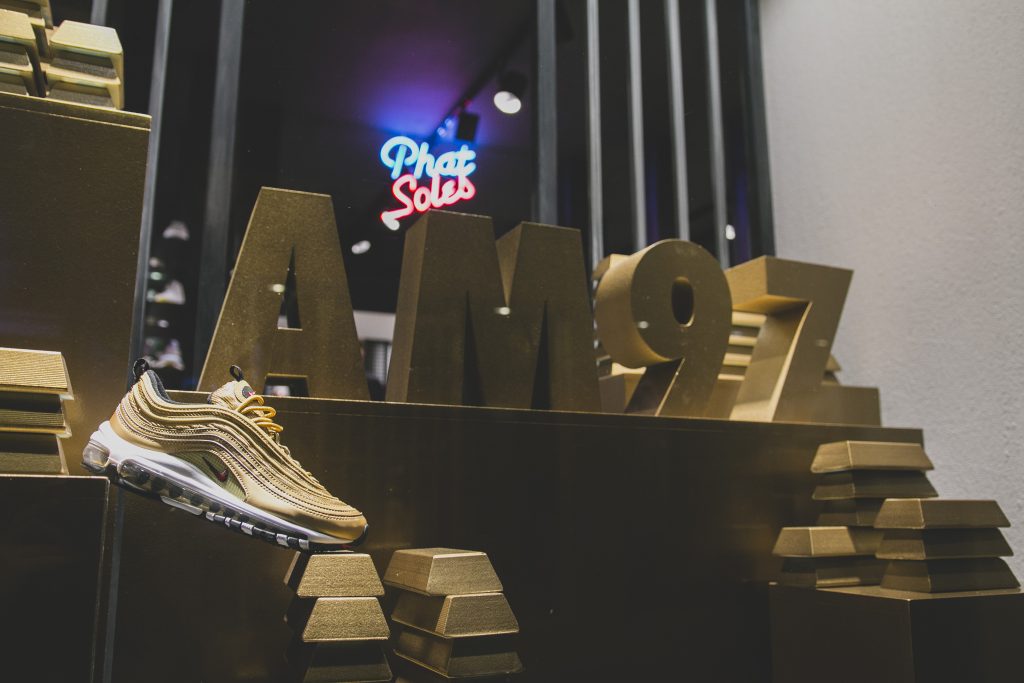 Ένα χρυσό αθλητικό παπούτσι Nike Air Max 97 Metallic Gold σε βιτρίνα καταστήματος.