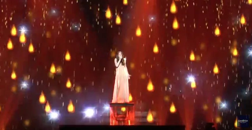 Η Demy στη σκηνή της Eurovision με φόντο χρυσές σταγόνες.
