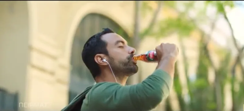 Ο Σάκης Τανιμανίδης πίνει Coca-Cola σε εξωτερικό χώρο.