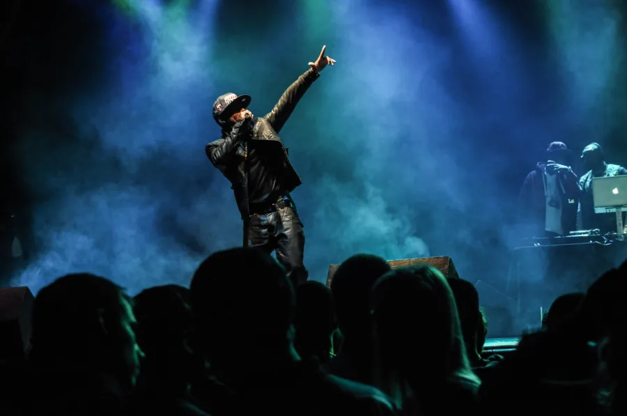 Hip-hop καλλιτέχνης στη σκηνή με υψωμένο το χέρι μπροστά σε κοινό.