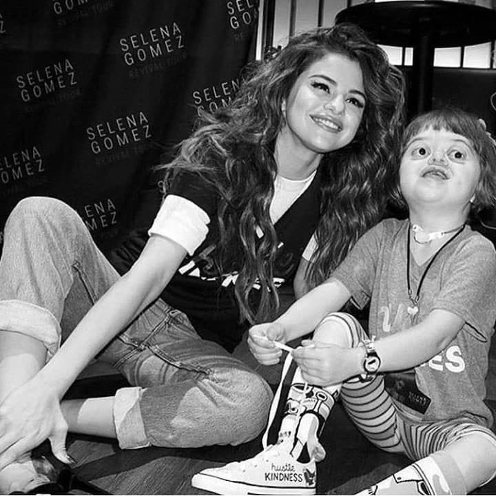 Η Selena Gomez χαμογελάει καθισμένη στο πάτωμα δίπλα σε ένα μικρό κορίτσι.