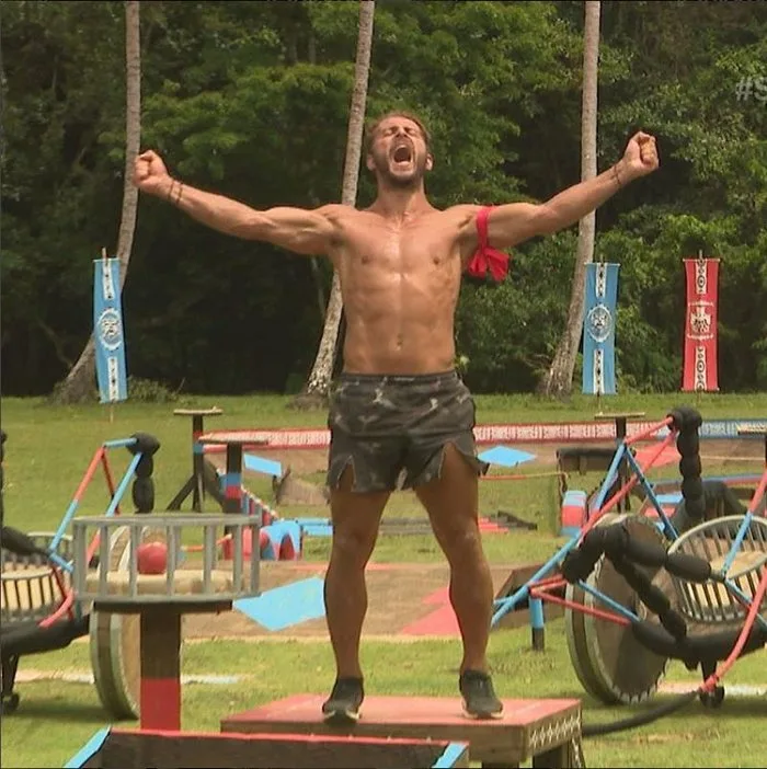Παίκτης του Survivor πανηγυρίζει με υψωμένα χέρια σε στίβο μάχης.