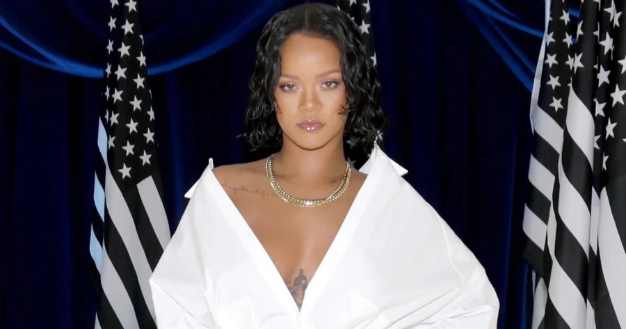 Η Rihanna με λευκό πουκάμισο μπροστά από αμερικανικές σημαίες.