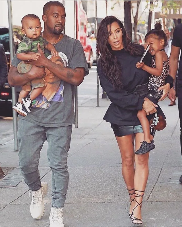 Η Kim Kardashian και ο Kanye West περπατούν στο δρόμο κρατώντας τα παιδιά τους.