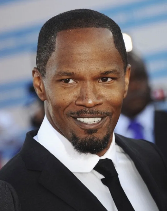 Ο Jamie Foxx χαμογελάει φορώντας μαύρο κοστούμι και λευκό πουκάμισο.