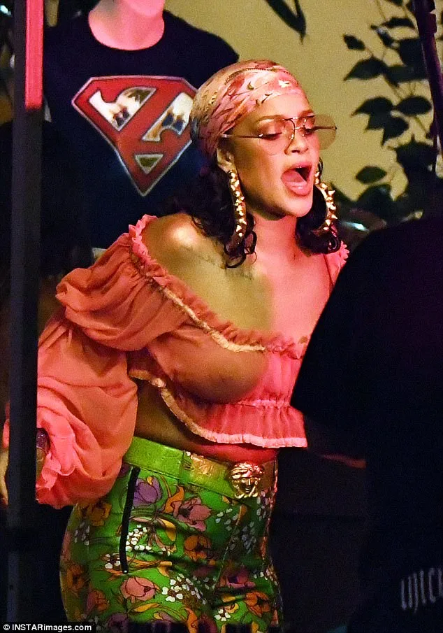 Η Rihanna με ροζ crop top, εμπριμέ παντελόνι και μαντήλι στο κεφάλι.