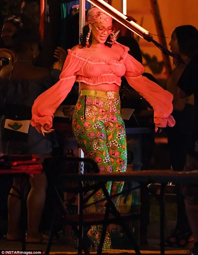 Η Rihanna με ροζ crop top και φλοράλ παντελόνι χορεύει σε εξωτερικό χώρο.