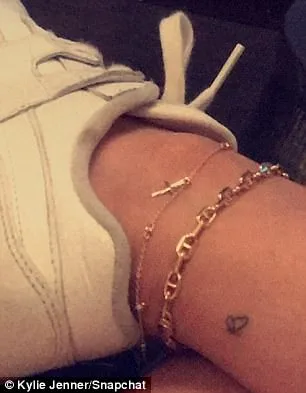 Κοντινό πλάνο στον αστράγαλο της Kylie Jenner με μικρό τατουάζ πεταλούδα και χρυσές αλυσίδες.