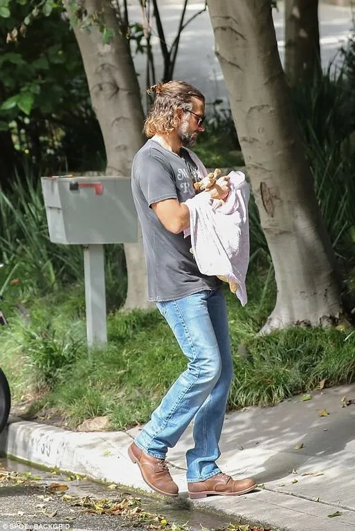 Ο Bradley Cooper κρατάει το μωρό του στην αγκαλιά του ενώ περπατάει στο δρόμο.