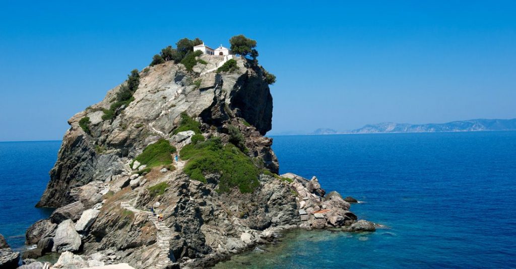 Το εκκλησάκι του Αγίου Ιωάννη του Ριγολόγου στην Σκόπελο, τόπος γυρισμάτων του Mamma Mia, με φόντο το γαλάζιο του Αιγαίου.