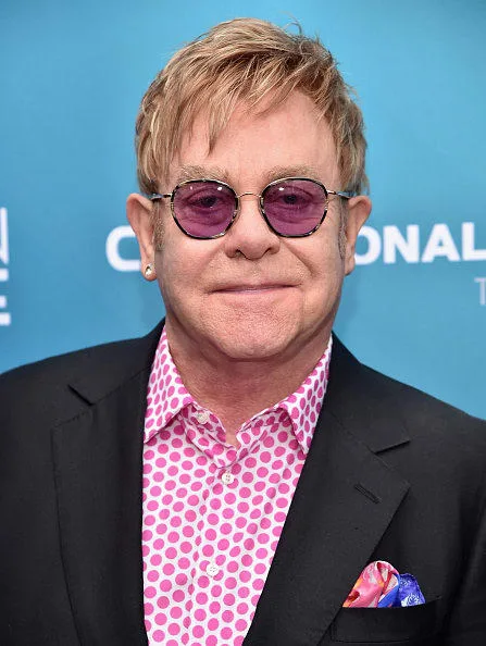 Ο Elton John με ροζ γυαλιά ηλίου και πουκάμισο με βούλες.