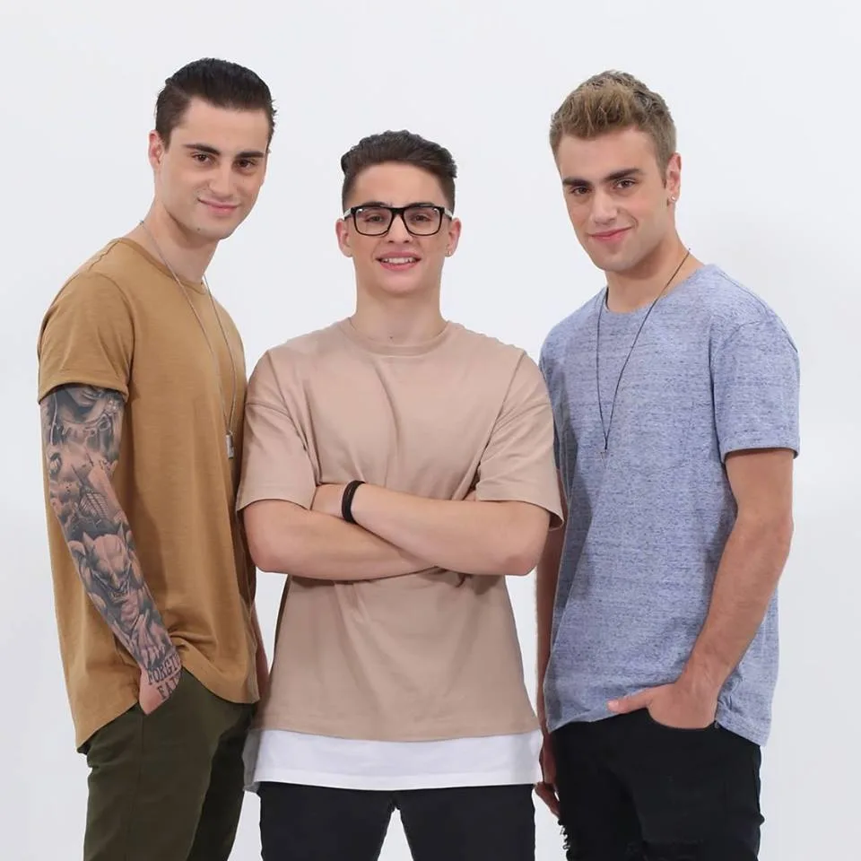 Τρία μέλη ενός boy band ποζάρουν σε λευκό φόντο.