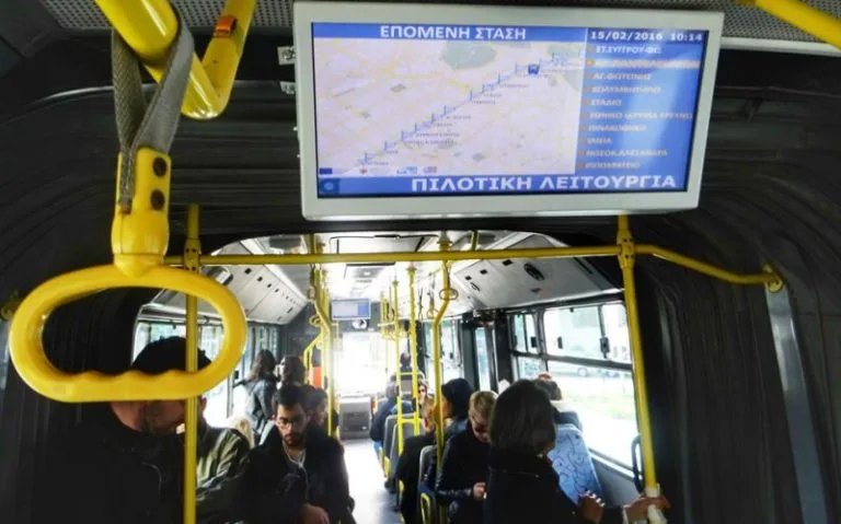 Εσωτερικό λεωφορείου του ΟΑΣΑ με οθόνη τηλεματικής και επιβάτες.