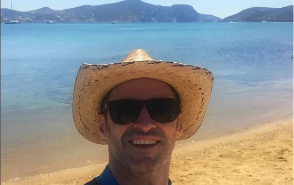 Ο Hugh Jackman με ψάθινο καπέλο και γυαλιά ηλίου σε παραλία.