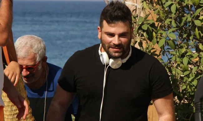 Ο Παντελής Παντελίδης με λευκά ακουστικά στον λαιμό σε εξωτερικό χώρο.