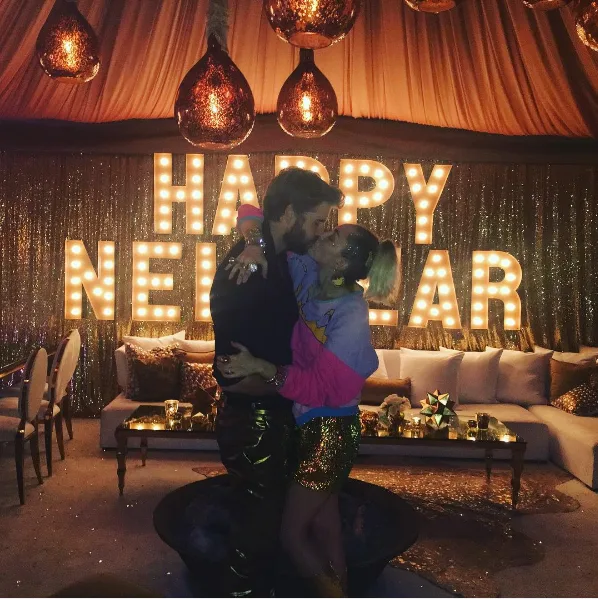 Η Miley Cyrus και ο Liam Hemsworth φιλιούνται μπροστά από φωτεινή επιγραφή Happy New Year.