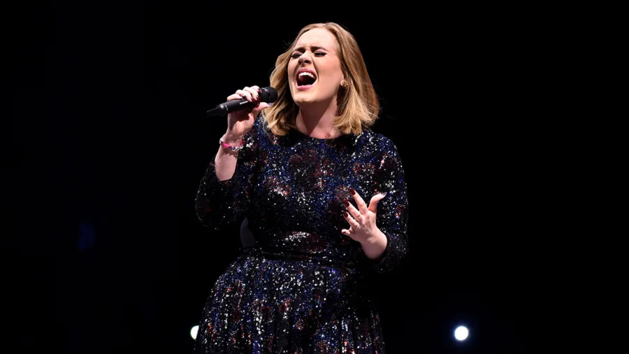 Η Adele τραγουδάει στη σκηνή με μαύρο φόρεμα με παγιέτες.