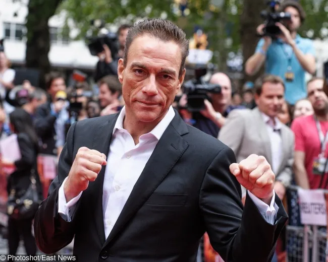 Ο Jean-Claude Van Damme σε κόκκινο χαλί με υψωμένες γροθιές.