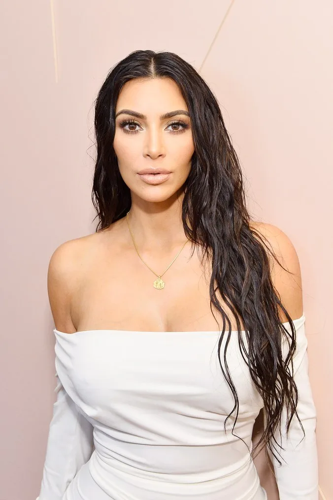 Η Kim Kardashian με λευκό off-the-shoulder φόρεμα και μακριά κυματιστά μαλλιά.