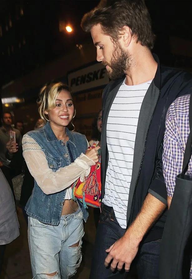 Η Miley Cyrus και ο Liam Hemsworth περπατούν μαζί το βράδυ.