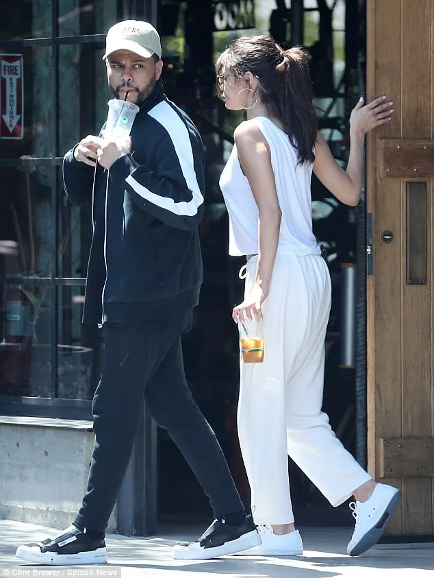 Η Selena Gomez και ο The Weeknd περπατούν στο δρόμο κρατώντας ροφήματα.