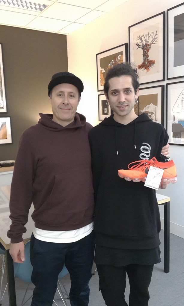 Ο Αλέξανδρος Excrusio με στέλεχος της Nike κρατώντας ένα πορτοκαλί αθλητικό παπούτσι.