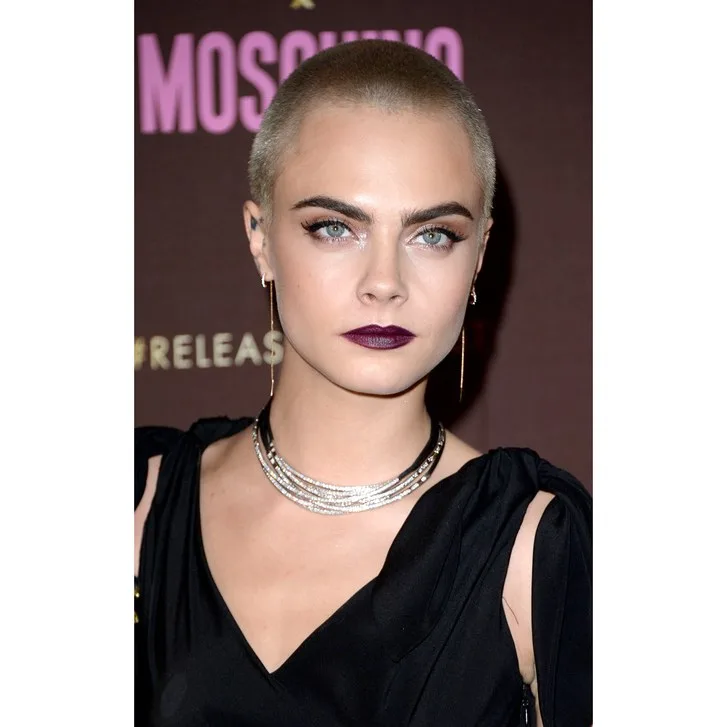 Η Cara Delevingne με ξυρισμένο κεφάλι και σκούρο κραγιόν σε εκδήλωση.