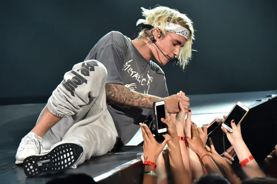 Ο Justin Bieber σε συναυλία του, καθισμένος στη σκηνή να κρατάει τα χέρια θαυμαστών.
