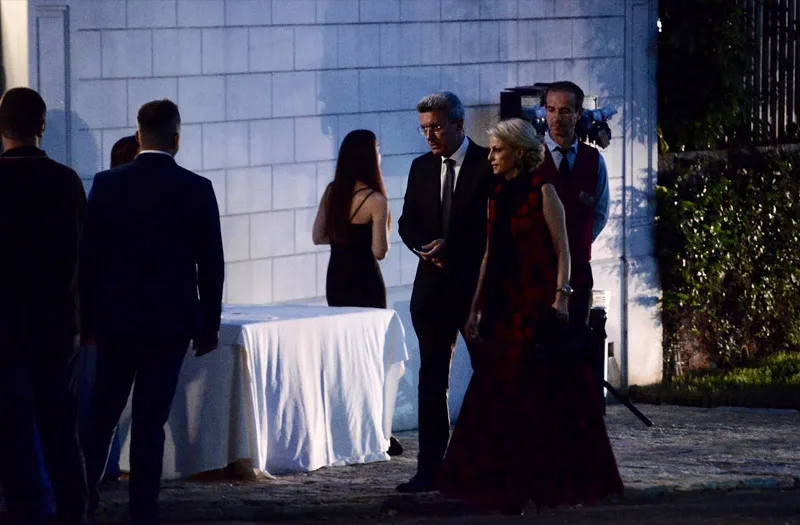 Καλεσμένοι σε γαμήλια δεξίωση δίπλα σε τραπέζι με λευκό τραπεζομάντιλο.