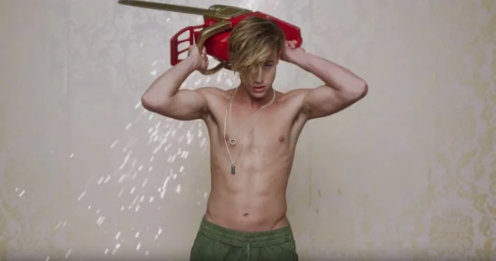 Ο Lucky Blue Smith κρατάει ένα αλυσοπρίονο πάνω από το κεφάλι του στο βίντεο κλιπ Boys της Charli XCX.