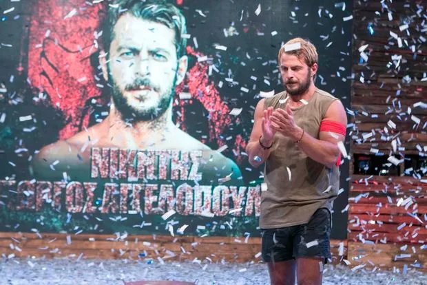 Άνδρας σε σκηνή με κομφετί μπροστά από μεγάλη αφίσα του εαυτού του.
