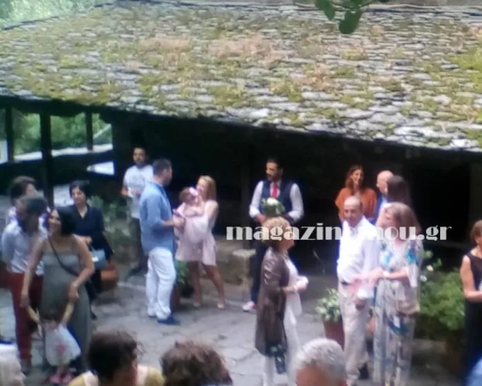 Ομαδική φωτογραφία από γάμο σε εξωτερικό χώρο με παραδοσιακή πέτρινη στέγη.