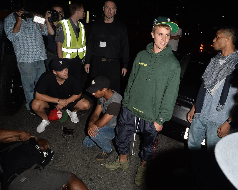 Ο Justin Bieber στέκεται δίπλα σε έναν τραυματισμένο φωτογράφο στο έδαφος μετά από ατύχημα με το αυτοκίνητό του.