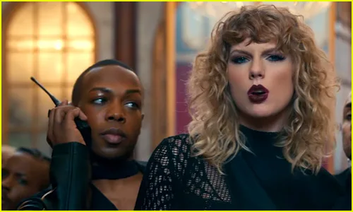 Η Taylor Swift με σγουρά μαλλιά και σκούρο κραγιόν δίπλα σε άνδρα με ασύρματο.