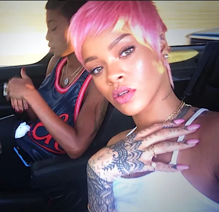 Η Rihanna με κοντά ροζ μαλλιά και τατουάζ στο χέρι μέσα σε αυτοκίνητο.