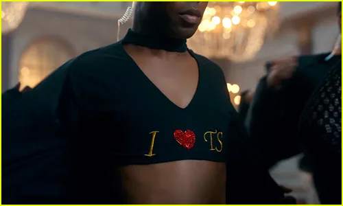 Χορευτής με μαύρο crop top που γράφει 'I ❤️ TS' σε video clip της Taylor Swift.