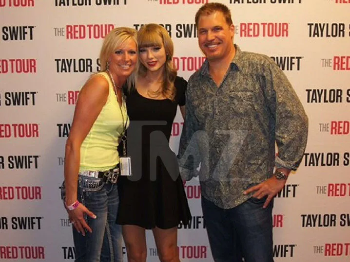 Η Taylor Swift ποζάρει με δύο άτομα μπροστά από φόντο The Red Tour.