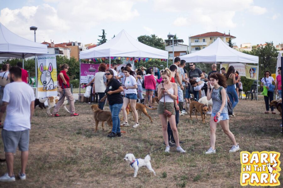 Κόσμος με τους σκύλους τους σε υπαίθρια εκδήλωση με λευκές τέντες.