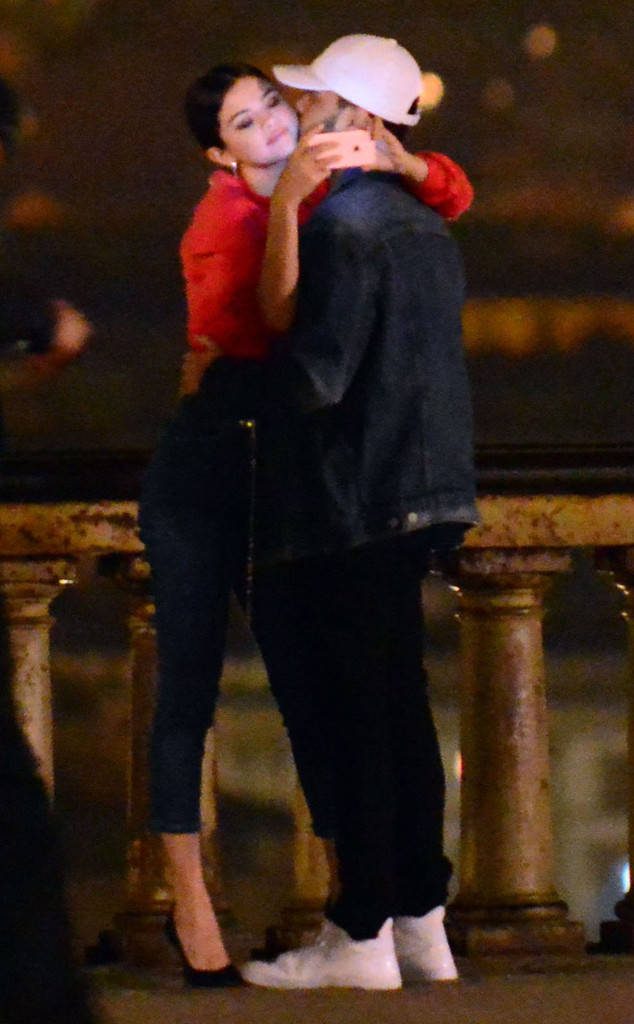 Η Selena Gomez και ο The Weeknd σε τρυφερή στιγμή σε γέφυρα τη νύχτα.