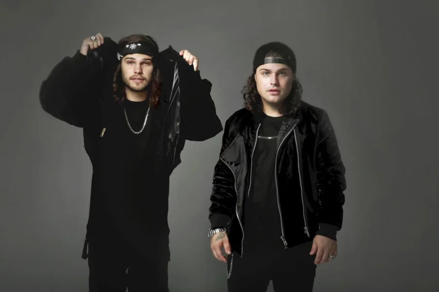 Οι DVBBS ποζάρουν με μαύρα ρούχα σε γκρίζο φόντο.