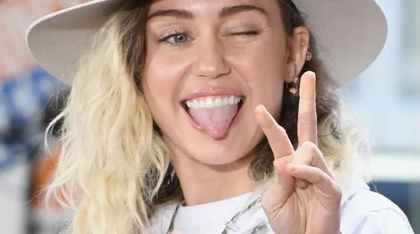 Η Miley Cyrus με καπέλο κλείνει το μάτι και κάνει το σήμα της ειρήνης.