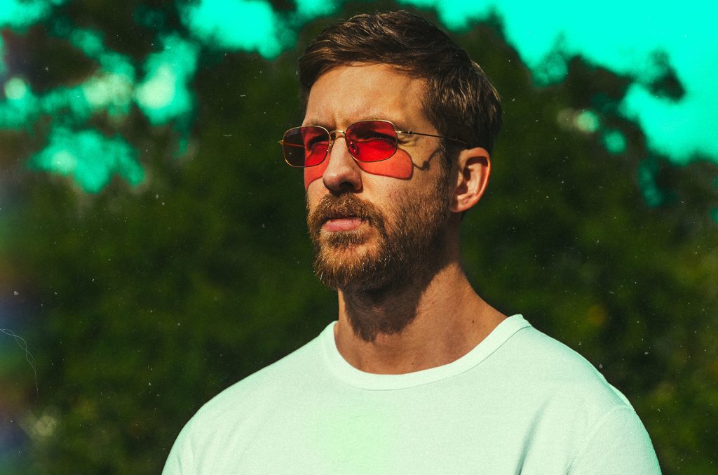 Ο Calvin Harris με κόκκινα γυαλιά ηλίου και μούσι σε εξωτερικό χώρο.