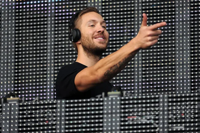 Ο Calvin Harris σε DJ set με ακουστικά και το χέρι υψωμένο.