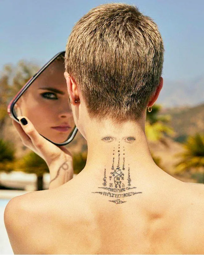Η Cara Delevingne με κοντό μαλλί δείχνει το τατουάζ με τα μάτια στον αυχένα της.