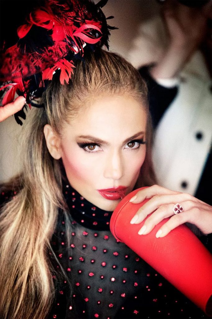 Η Jennifer Lopez με εντυπωσιακό καπέλο με κόκκινα φτερά και μαύρο διάφανο ρούχο.