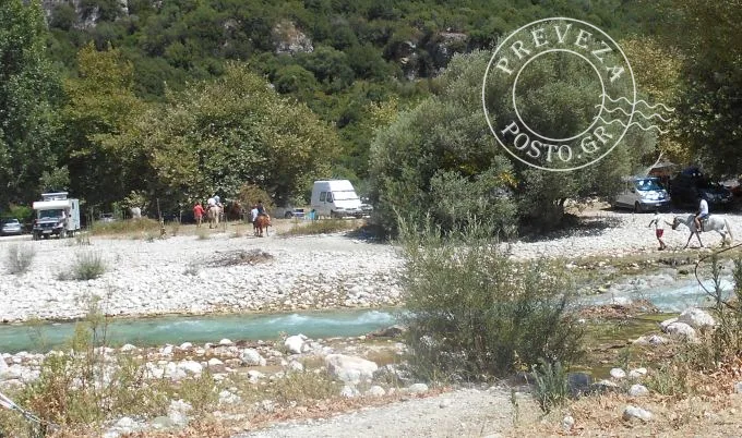 Άνθρωποι με άλογα δίπλα σε ποτάμι και τροχόσπιτα.