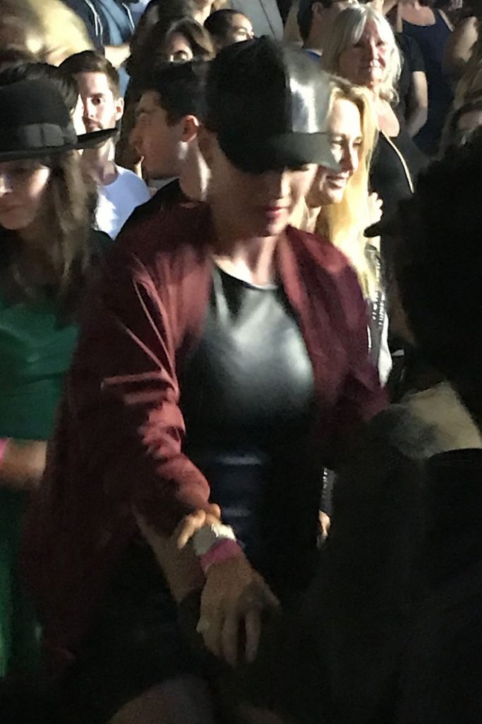 Η Katy Perry με μαύρο καπέλο και μπορντό ζακέτα ανάμεσα σε πλήθος.