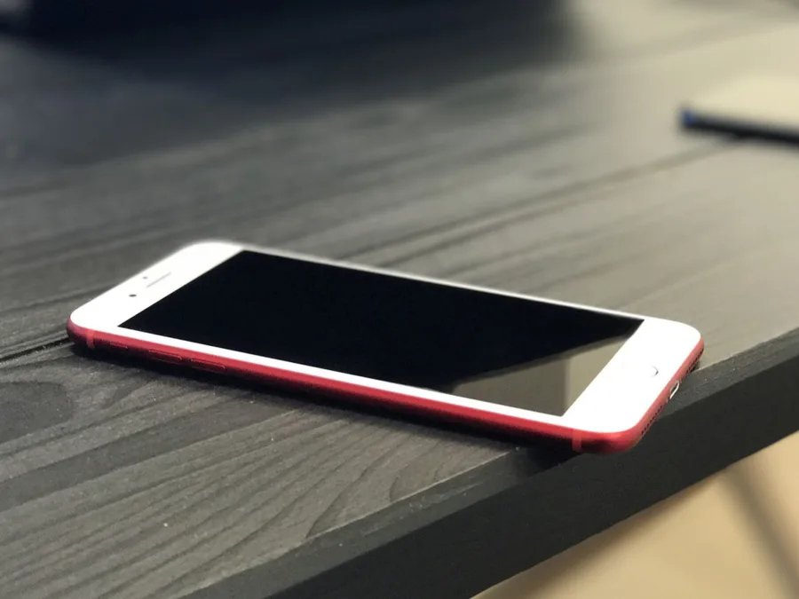 Ένα κόκκινο iPhone τοποθετημένο πάνω σε μια σκούρα ξύλινη επιφάνεια.