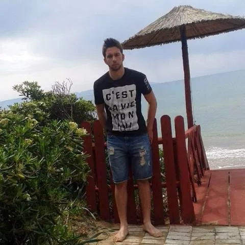 Νεαρός άνδρας με μαύρο t-shirt και τζιν βερμούδα σε παραλία.